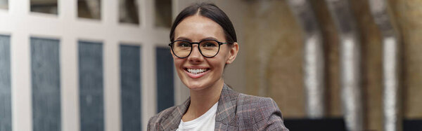 Улыбающаяся деловая женщина, стоящая в современном офисе и смотрящая в камеру