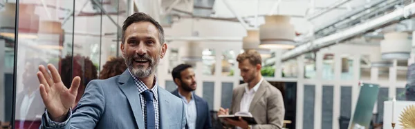 stock image Smiling businessman standing in office on colleagues background and waving hi. High quality photo