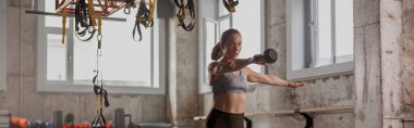 Spor giyim kuşağında genç ve narin bir bayan. Güzel bir atletik vücudu var. Spor salonunda kettlebell ile egzersiz yapıyor.