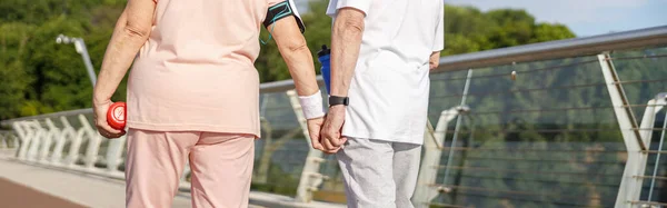 Seniorenpaar Trainingspakken Met Flessen Wandelingen Hand Hand Langs Voetgangersbrug Zomer — Stockfoto