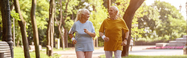 Happy mature woman with husband run together along road in picturesque park on summer day. Active lifestyle and healthcare
