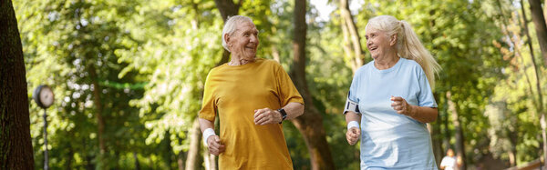 Positive senior family couple run together along road in green park on summer day. Active lifestyle and healthcare