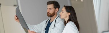 Üniformalı iki doktor klinikteki hastanın omurgasının röntgenini veya MRI taramasını tartışıyor.