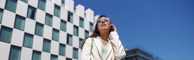 Attractive businesswoman in white suit walking on skyscrapers cityscape background