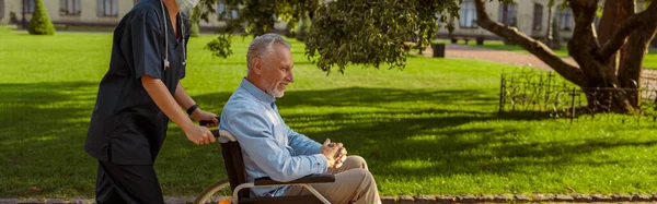 在医院附近的公园里散步时 全长的护士长与坐轮椅的老人在一起 医疗保险 康复概念 侧视图 — 图库照片