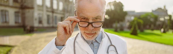 Portret Dojrzałego Lekarza Fartuchu Laboratoryjnym Ustawiającego Okulary Patrzącego Dokładnie Kamerę — Zdjęcie stockowe