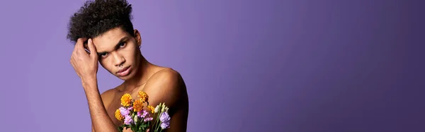 Transgender model posing with flowers. Portrait of athletic male with bouquet. Attractive young trans gender man on purple studio background with copy space. Professional shot with copyspace