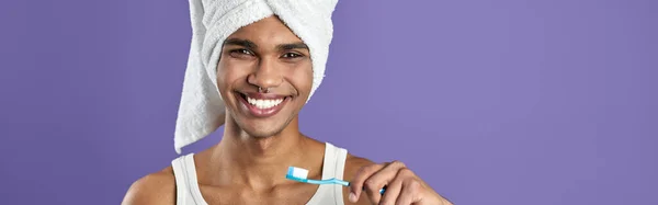 若いトランスジェンダーの男は紫色の背景の肖像画に隔離された歯を磨く 歯ブラシ室でアフロアメリカの男性を笑顔 頭部の健康歯科ケアのシャワータオルのスポーツマン — ストック写真