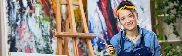 Radostná Malířka Zástěře Usmívající Kamery Držící Štětec Při Malování Sedící — Stock fotografie