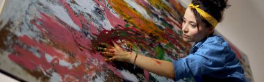 Odaklanmış genç kadın, kadın ressam büyük, modern, soyut bir yağlı boya tablosu yaratıyor, parmaklarıyla tuvale boya sürüyor. Sanat, hobi, eğlence konsepti