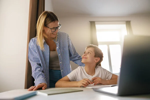 stock image Smiling mom helping her son doing homework studying online using laptop in home