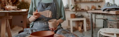 Sanat atölyesindeki çanak çömleği dekore ederken fırçayı akrilik boyaya batıran genç yaratıcı kadın.