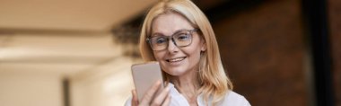 Çevrimiçi çağrı. Normal giyinen güzel bir son sınıf öğrencisi gülümseyip telefonda konuşurken akıllı telefonuyla evde dikiliyor. İnsanlar ve iletişim konsepti. Yatay çekim