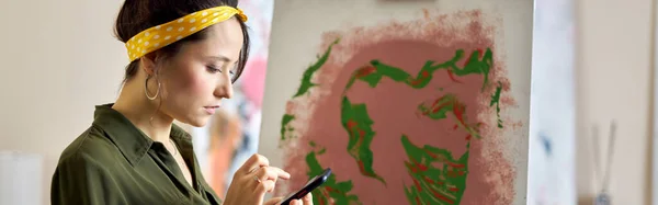 Focused Young Woman Using Her Smartphone While Creating Abstract Painting — Stock Photo, Image