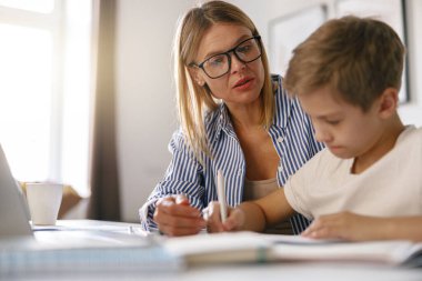 Odaklanmış bir anne, evdeki dizüstü bilgisayarla oğlunun ödevlerini yapmasına yardım ediyor.