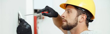 Portrait of male worker professional electrician in uniform installing electrical outlet in apartment after renovation work. Manual work, maintenance, occupation concept. Side view