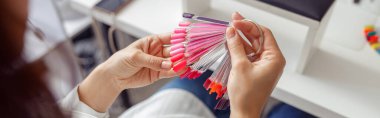 Back view of woman making choice the color of nail polish in salon of manicure