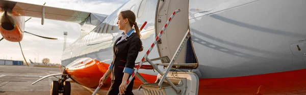 Full length of stewardess in aviation air hostess uniform standing on boarding stairs of private aircraft jet