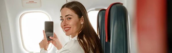 Radosna Podróżniczka Patrząca Kamerę Uśmiechnięta Podczas Lotu Samolotem Telefonem Komórkowym — Zdjęcie stockowe