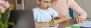 Güzel bir annenin portresi, küçük bir çocuğa ödev defterinde yardım ediyor. Yazma alıştırması.