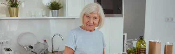 Hermosa Pensionista Femenina Mirando Cámara Sonriendo Mientras Prepara Comida Saludable —  Fotos de Stock