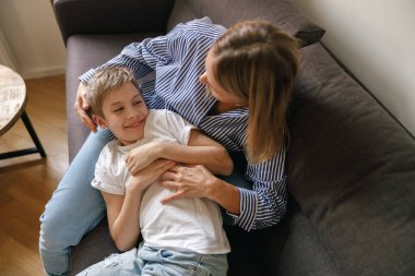 Anne ve oğlu evlerinde kanepede gıdıklanıyor. Mutlu annelik ve çocukluk