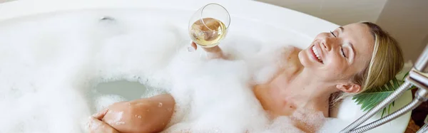 白ワインを飲みながら浴槽の泡の中に寝そべっている幸せな若い女性の幸せのトップビュー リラックスして — ストック写真