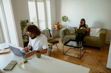 Bir erkek ve bir kadın evdeki oturma odasında çalışıyorlar. Mesafe çalışma kavramı