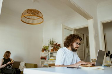 Genç bir çift evde dizüstü bilgisayar kullanıyor. Mesafe çalışma kavramı