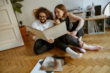 Zeminde oturan ve farklı plaklara sahip vinil çalarlarda müzik dinleyen çift.