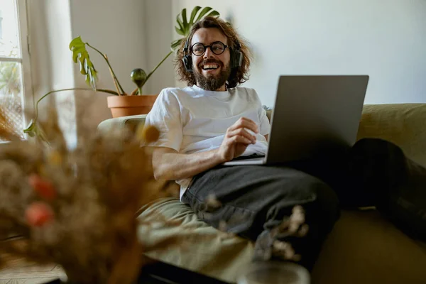 Pria Dengan Headphone Berbaring Sofa Nyaman Rumah Dan Menggunakan Laptop — Stok Foto