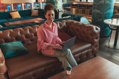 Kanepede rahat bir şekilde otururken dizüstü bilgisayarda çalışan serbest çalışan bir kadın. Yüksek kalite fotoğraf