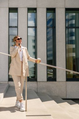 Gülümseyen kadın ofis çalışanı modern bina hakkında konuşuyor ve kahve içiyor.