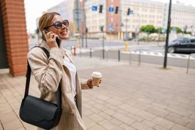 Smiling woman office worker is talking by phone while standing on modern building background 
