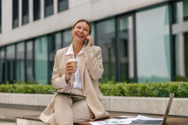 Businesswoman talking with client and work on laptop outside of office. Distance work concept