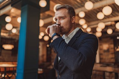 İş adamı, modern bir iş yerinde çalışırken kahve içiyor ve yan gözle bakıyor.