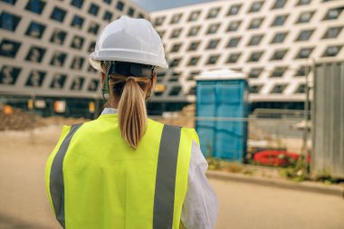 İnşaat arka planında koruyucu miğferli kadın mühendisin arka görüntüsü 