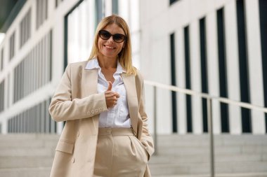 Gülümseyen kadın ofis çalışanı modern binanın arka planında duruyor ve kameraya bakıyor.
