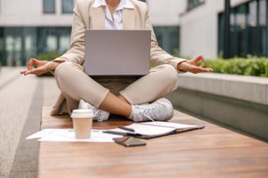Nilüfer pozisyonunda oturan odaklanmış kadın yönetici ve çevrimiçi iş arasında meditasyon