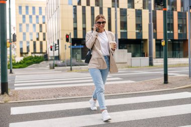Gülümseyen kadın ofis çalışanı modern bina hakkında konuşuyor ve kahve içiyor.