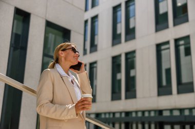 Gülümseyen kadın ofis çalışanı modern bina hakkında konuşuyor ve kahve içiyor.