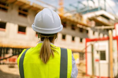 İnşaat arka planında koruyucu miğferli kadın mühendisin arka görüntüsü 