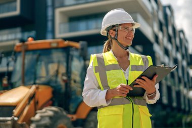 Gülümseyen kadın tasarım mimarı inşaat sırasında binayı incelerken notlar alıyor. 