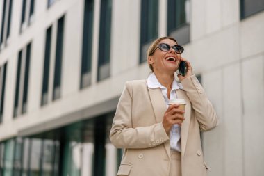 Gülümseyen kadın ofis çalışanı modern bina hakkında konuşuyor ve kahve içiyor.
