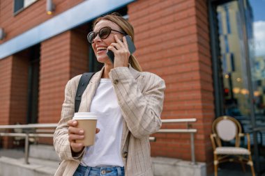 Gülümseyen kadın ofis çalışanı modern bina hakkında konuşuyor ve kahve içiyor.