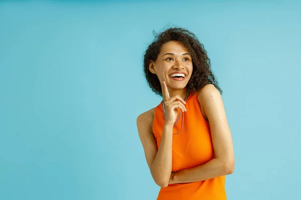Usmívající Žena Oranžových Šatech Dotýká Tváře Dívá Straně Modrém Pozadí — Stock fotografie
