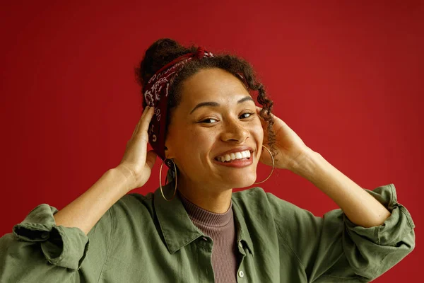 Usmívající Žena Dotýká Vlasů Dívá Kameru Stojící Červeném Pozadí Studia — Stock fotografie