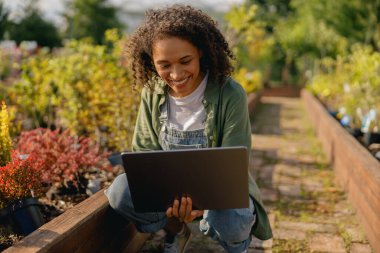 Kadın bahçıvan, bitki merkezinin arka planında otururken dizüstü bilgisayarda çalışıyor. Yüksek kalite fotoğraf