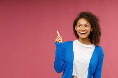 Pozitif kadın kırmızı stüdyo arka planında gülümsemeyle yan tarafı işaret ediyor. Yüksek kalite fotoğraf