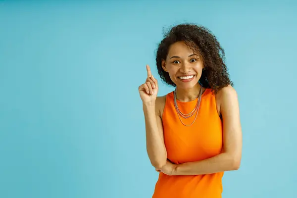 Pozitivní Žena Oranžových Šatech Ukazuje Prstem Nahoru Úsměvem Modrém Pozadí — Stock fotografie